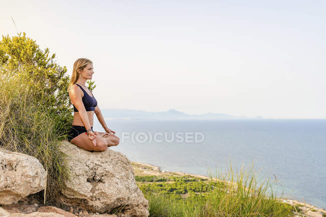 Reife Frau meditiert auf Felsen an Klippe — Stockfoto