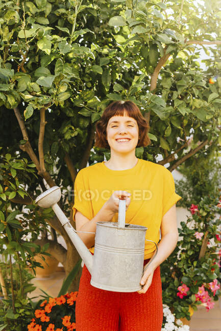 Smiling woman with watering can standing in front of lemon tree at garden — Stock Photo