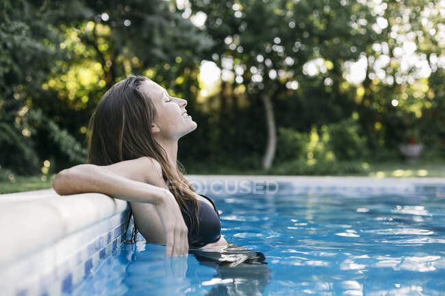 Mujer joven con los ojos cerrados relajándose junto a la piscina - foto de stock