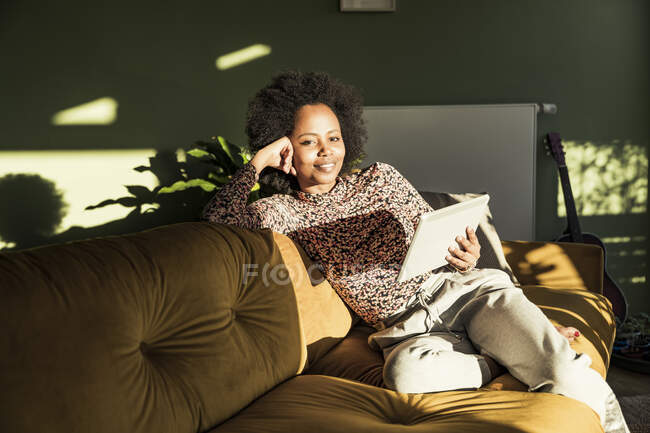 Woman holding digital tablet while sitting in living room — Stock Photo