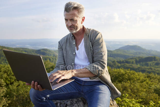Man using laptop while sitting on mountain — Stock Photo