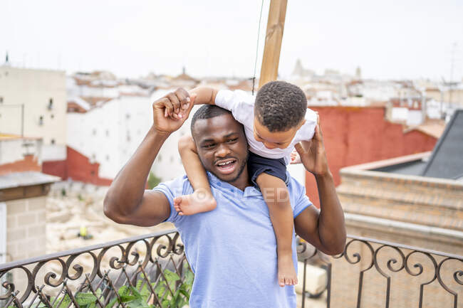 Грайливий батько носить сина на плечах у балконі. — стокове фото