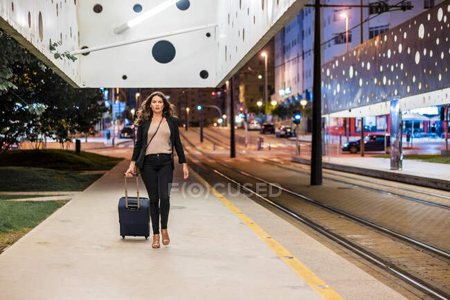Деловая женщина таскает колесный багаж во время прогулки по платформе ночью — стоковое фото
