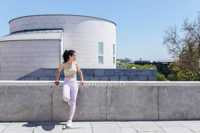 Sportlerin schaut bei sonnigem Tag weg, während sie sich an Stützmauer lehnt — Stockfoto