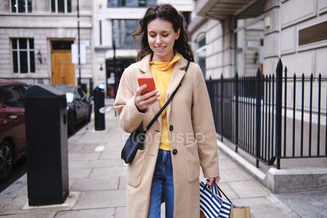 Donna sorridente che utilizza lo smart phone mentre fa shopping in città — Foto stock