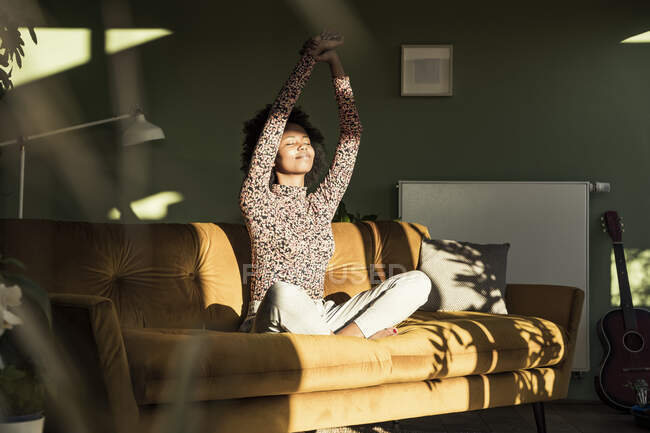 Frau mit erhobenen Händen sitzt zu Hause auf Sofa — Stockfoto