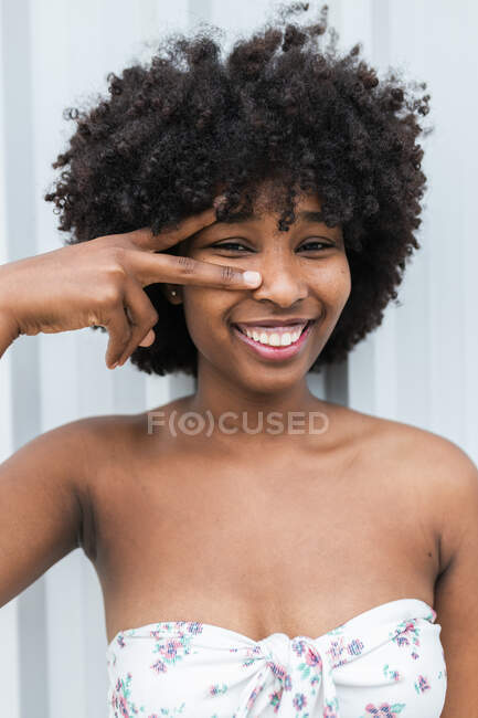 Smiling young woman doing peace gesture in front of wall — Stock Photo