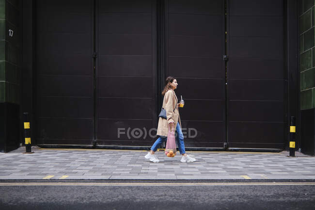 Junge Frau läuft auf Fußweg an schwarzer Tür vorbei — Stockfoto