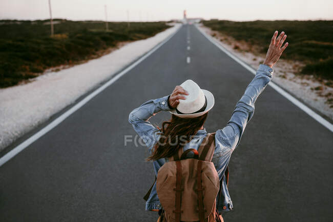 Backpacker with hand raised standing on road — Stock Photo