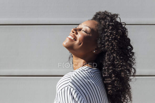 Lächelnde Bwoman mit geschlossenen Augen an sonnigen Tagen an der Wand stehend — Stockfoto