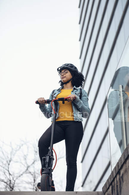 Mujer de pie con scooter de empuje eléctrico fuera del edificio - foto de stock