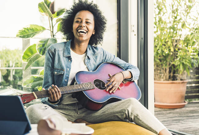 Mujer alegre tocando la guitarra mientras se sienta en casa - foto de stock