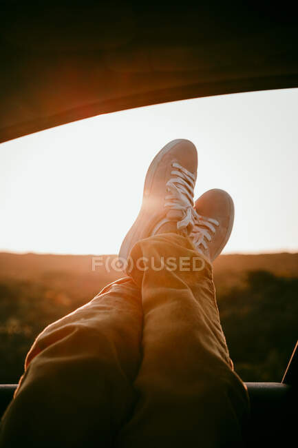 Woman with legs crossed at ankle on car window during sunset — Stock Photo