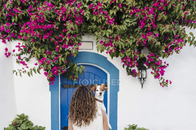 Woman with dog in front of flowering plant on wall — Stock Photo