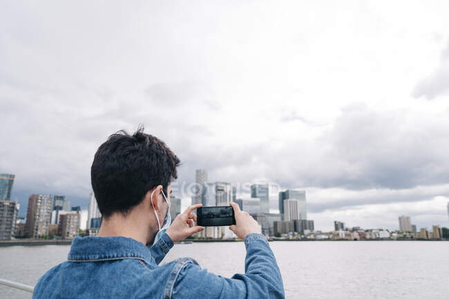 Joven fotografiando a través del teléfono móvil durante COVID-19 - foto de stock