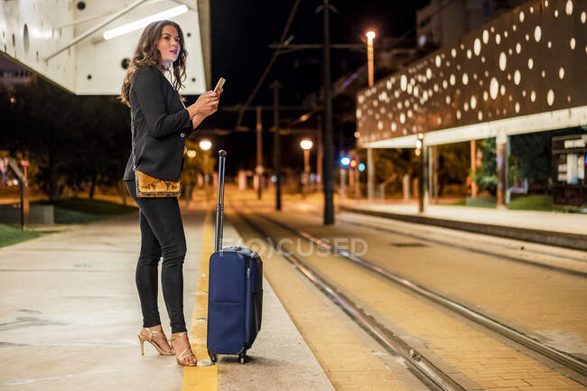 Professionista femminile guardando lontano mentre tiene il telefono cellulare alla stazione del tram — Foto stock