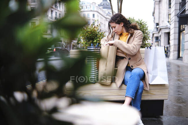 Donna in cerca di borse della spesa mentre seduto sulla panchina a piedi — Foto stock