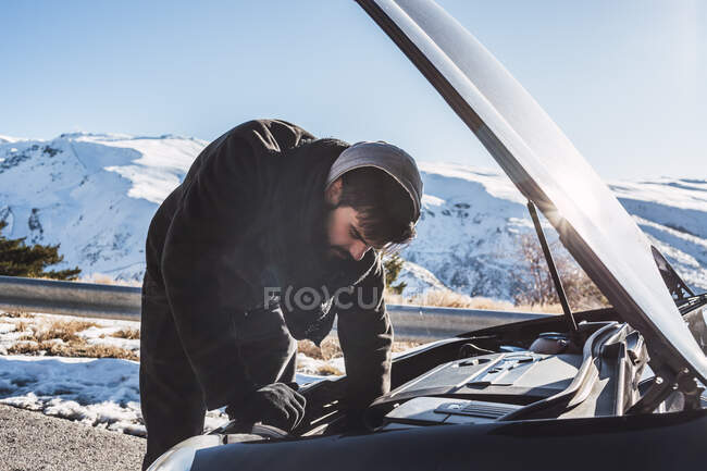 Uomo riparazione auto su terreni innevati contro il cielo durante l'inverno — Foto stock