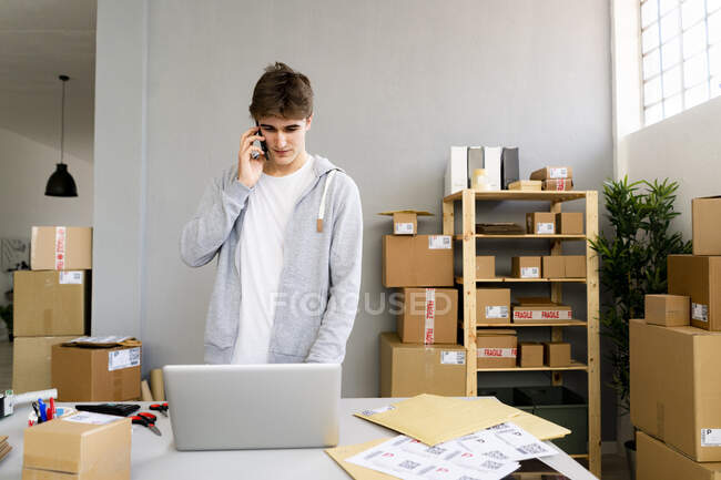 Бизнесмен разговаривает по мобильному телефону во время работы на ноутбуке в офисе — стоковое фото