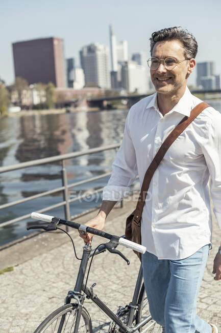 Улыбающийся бизнесмен, гуляющий на велосипеде в солнечный день — стоковое фото
