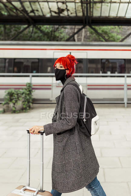 Donna dai capelli rossi con maschera protettiva che cammina alla stazione ferroviaria — Foto stock