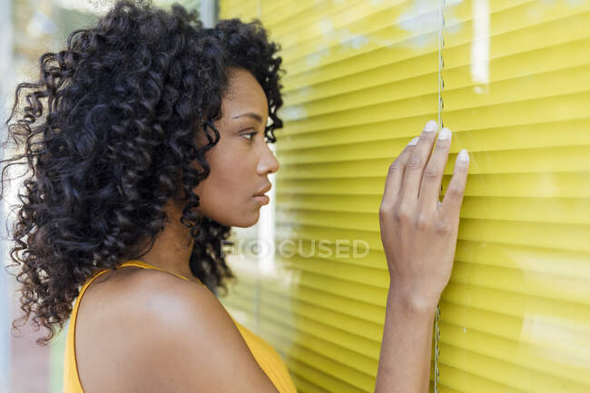 Young woman with curly hair touching yellow window — Stock Photo