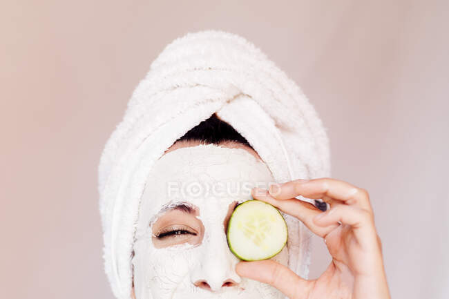 Mujer joven con máscara facial de belleza que cubre el ojo con rodaja de pepino - foto de stock