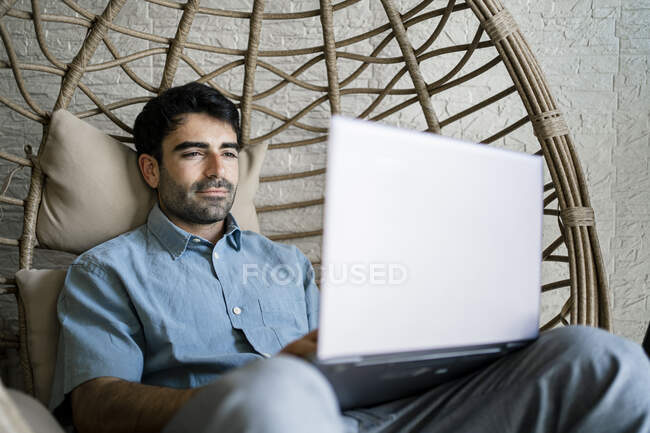Male freelancer using laptop while sitting on chair swing in cafe — Stock Photo