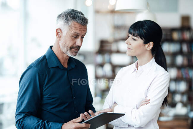 Female entrepreneur listening to colleague standing with digital table in coffee shop — Stock Photo