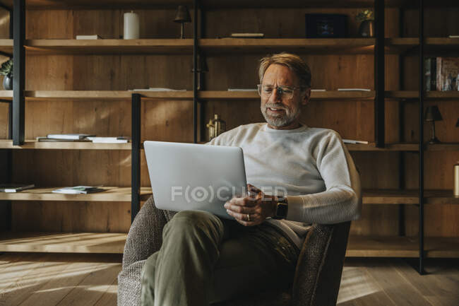 Reifer Mann benutzt Laptop, während er auf Sessel sitzt — Stockfoto
