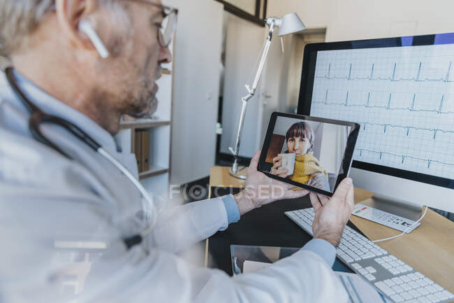 Hausarzt im Gespräch mit Patient auf Videotelefonie über digitales Tablet in Arztpraxis — Stockfoto