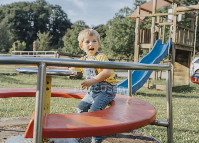 Charming boy sitting on merry go round in playground — Stock Photo