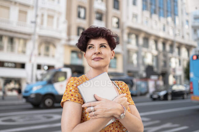 Mujer contemplando mientras sostiene la tableta digital en la ciudad - foto de stock