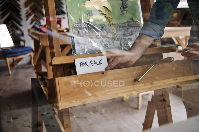 Masculino loja proprietário mantendo para venda sinal na frente de pintura visto através de janela de vidro — Fotografia de Stock
