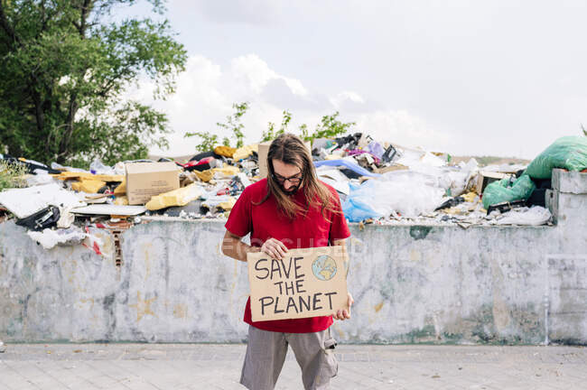 Mann hält Pappe vor Müllhalde — Stockfoto