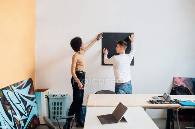 Giovane coppia attaccare cartone a parete in studio — Foto stock