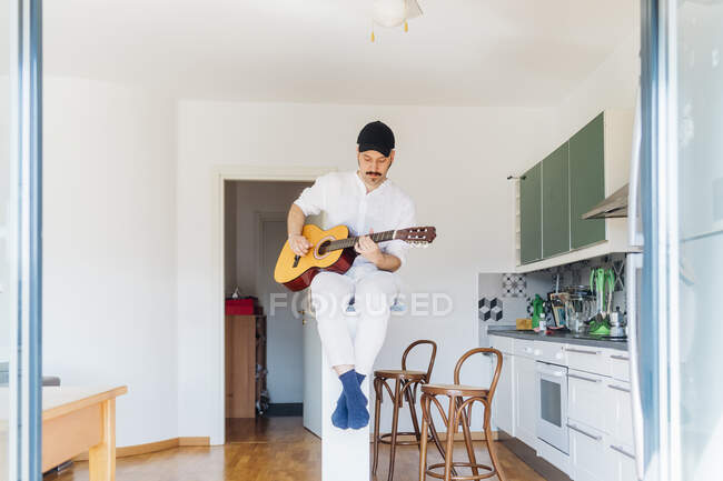 Guitariste masculin portant une casquette jouant de la guitare à la cuisine — Photo de stock