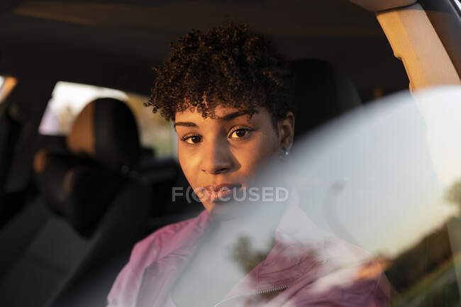 Кучерява жінка сидить у машині під час заходу сонця. — стокове фото