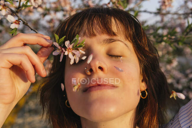 Smiling woman holding almond blossom branch by eyes during sunset — Stock Photo