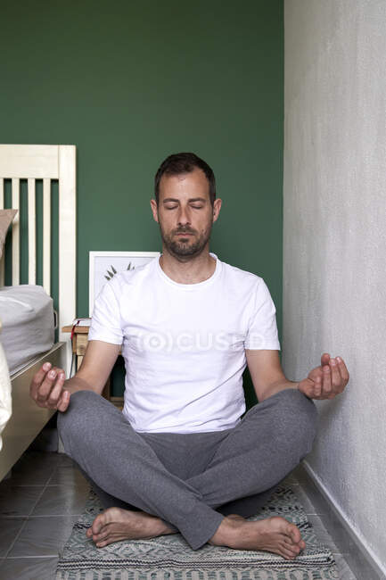 Mitte erwachsener Mann praktiziert Yoga, während er im Schlafzimmer sitzt — Stockfoto