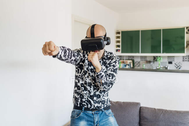 Young man wearing virtual reality simulator punching at home — Stock Photo