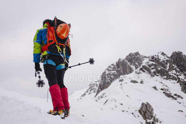 Mature man carrying backpack while walking on snowcapped mountain with crampon and hiking poles — Stock Photo
