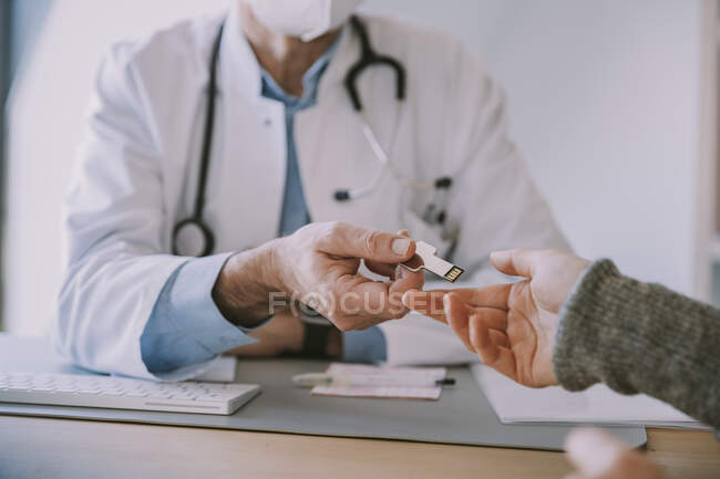 Medico che dà USB bastone al paziente mentre seduto a tavola presso lo studio del medico — Foto stock