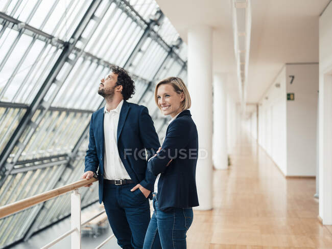 Smiling businesswoman with arms crossed standing by colleague at office corridor — Stock Photo
