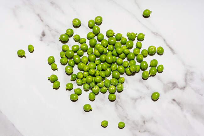 Raw green peas lying on marble surface — Stock Photo