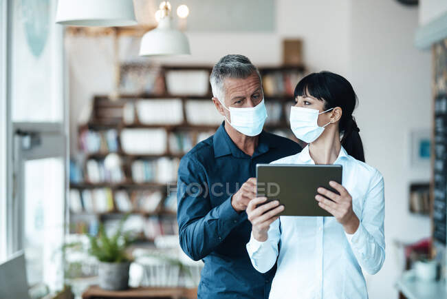 Propietarios masculinos y femeninos con máscara facial usando tableta digital en cafetería - foto de stock