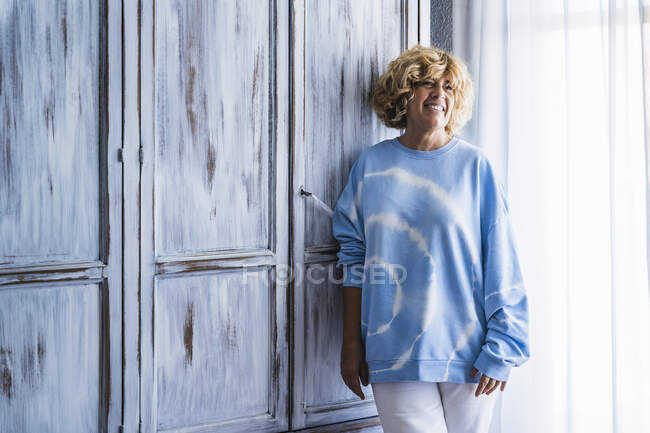 Donna sorridente in piedi vicino all'armadio di legno a casa — Foto stock