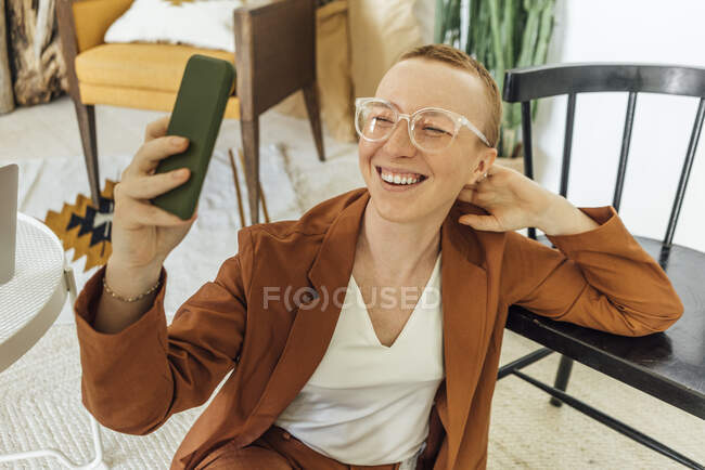 Happy young businesswoman taking selfie through smart phone at work place — Stock Photo