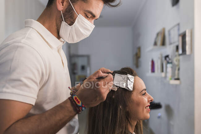 Чоловічий експерт з масками обличчя, який фарбує посміхаючись жіноче волосся в салоні — стокове фото