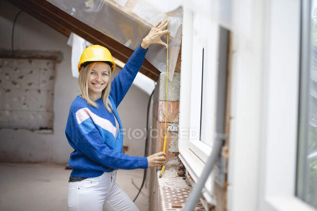 Lächelnde Bauunternehmerin beim Messen mit Zollstock auf der Baustelle — Stockfoto